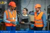 Three individuals in orange safety vests and hard hats standing in an industrial setting, with one holding a clipboard and another holding a cardboard box.